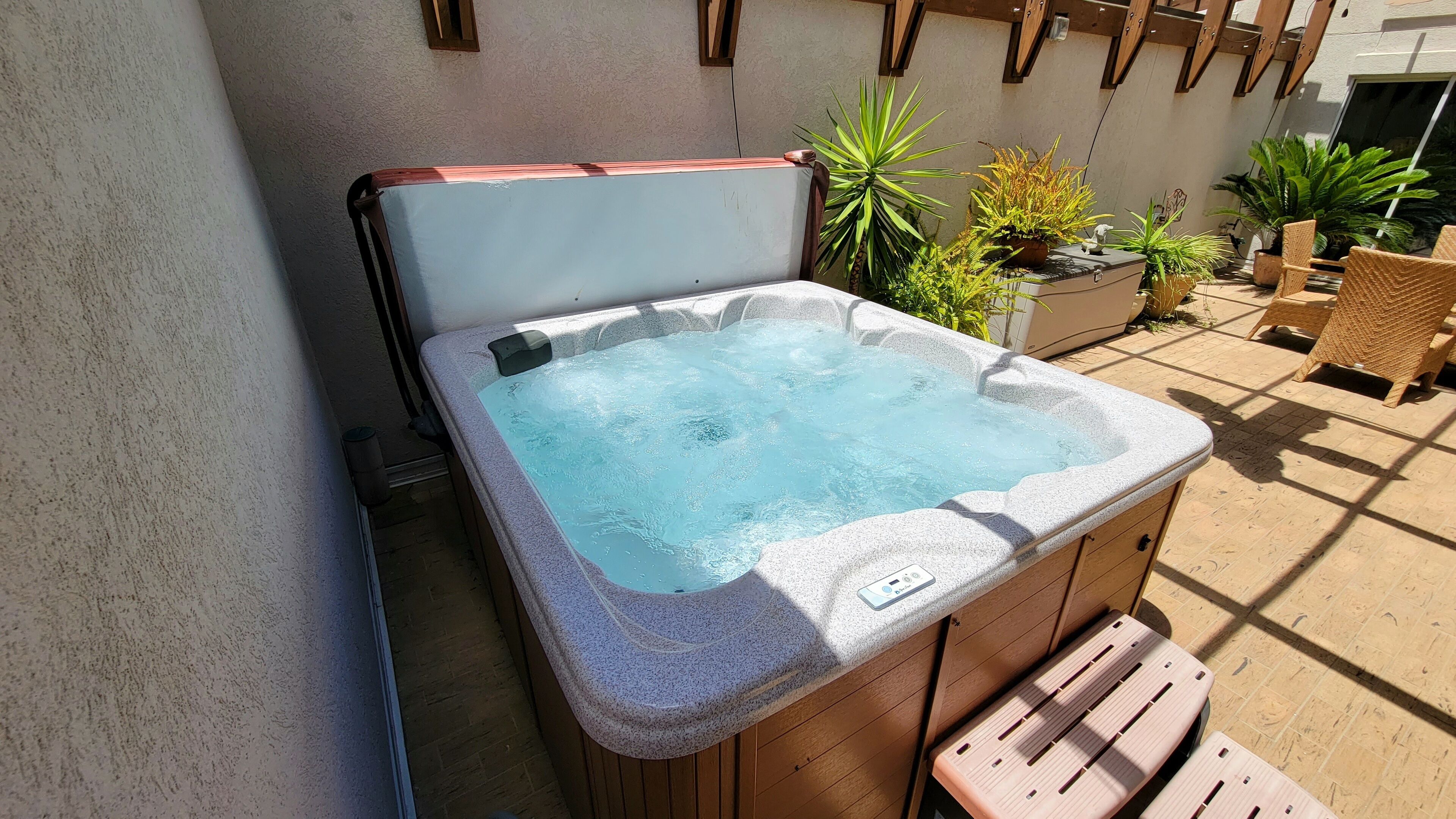 Een hottub met een stenen buitenkant, houten banken en plantenbakken op de achtergrond.