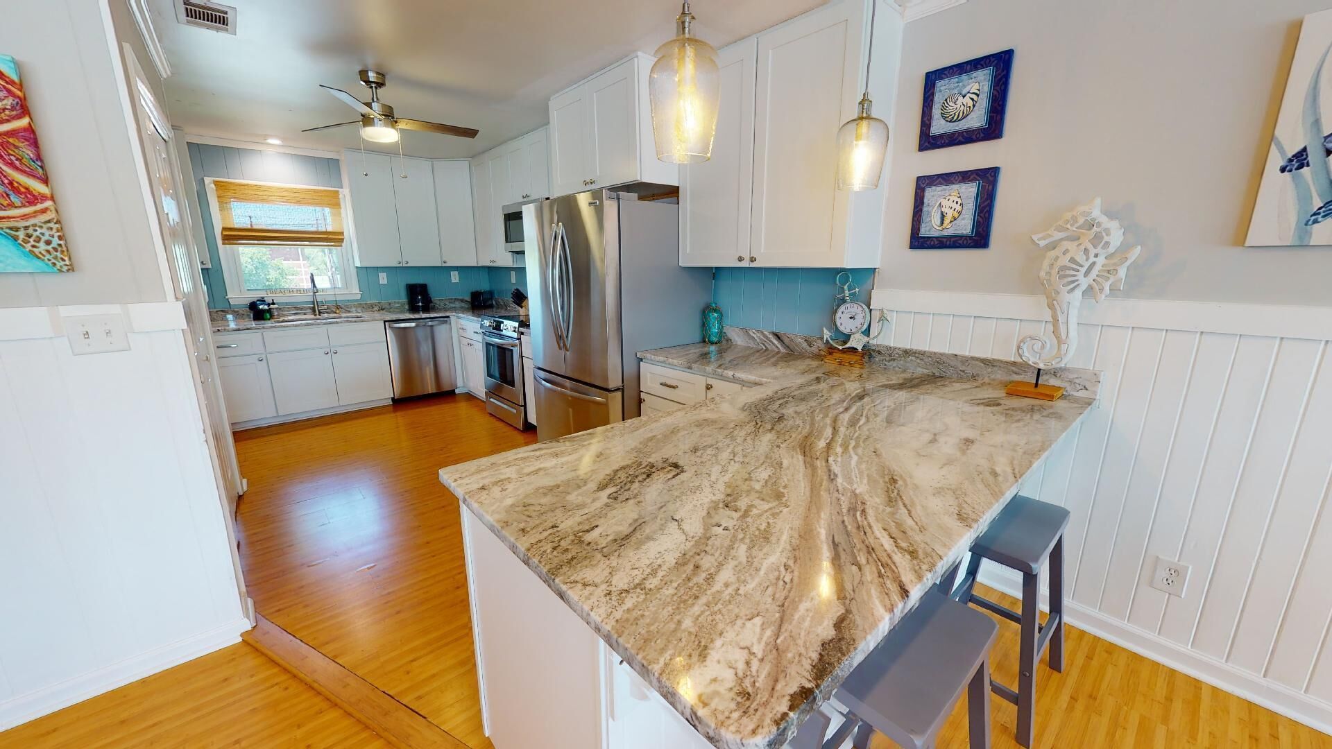 A modern kitchen with white cabinets, a marble countertop, stainless steel appliances, and pendant lighting.