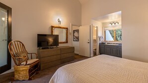 Quarto com uma cama grande, cômoda, televisão e uma cadeira.