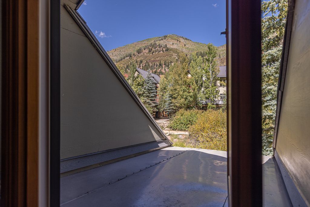 A view from a window with a mountain in the background, a house, and some trees.