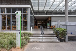 Un edificio moderno con fachada de vidrio, un letrero verde con una cámara y una escalera que lleva a la entrada.