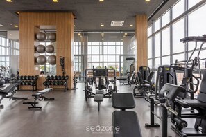 A gym with various exercise equipment, large windows, and a wooden wall with exercise balls.