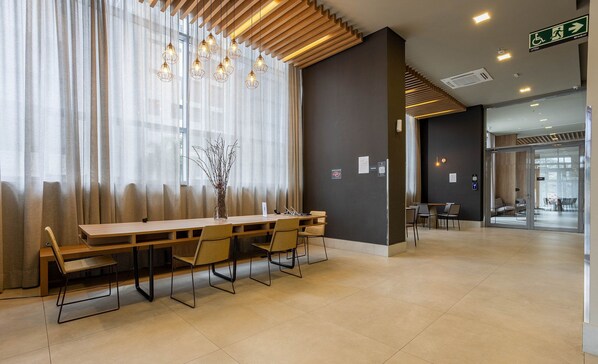 A modern hotel lobby with a wooden reception desk, chairs, and a large window with sheer curtains.
