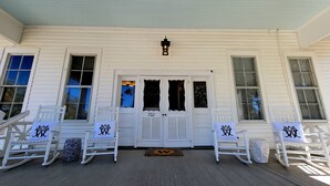 A white wooden house with a porch, two rocking chairs, and a door with the number 102. - The Wheel House by Tybee Vacation Rentals (Tybee Island)