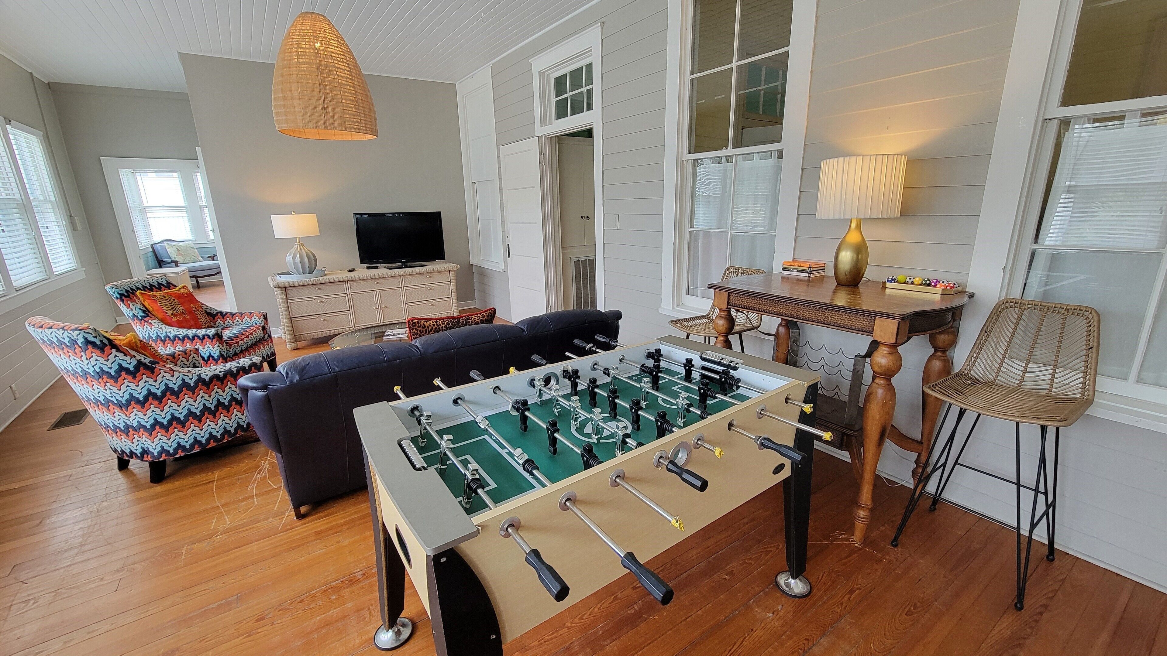 Een gezellige woonkamer met een tafelvoetbaltafel, een comfortabele bank, een televisie en een eethoek met een tafel en stoelen.