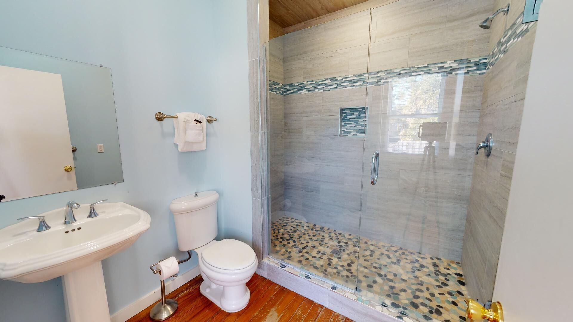 A bathroom with a shower, toilet, sink, and a mirror.