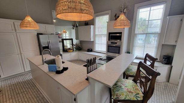 A modern kitchen with white cabinetry, a central island, and pendant lighting. - The Wheel House by Tybee Vacation Rentals (Tybee Island)