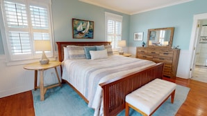 A bedroom with a large bed, wooden headboard, two bedside tables, a dresser, and a bench.