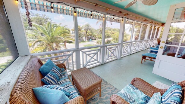 A covered outdoor seating area with wicker furniture and a view of palm trees.