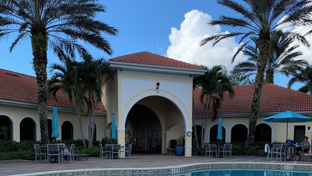 A pool area with a clear blue pool, palm trees, and a building with a red-tiled roof.