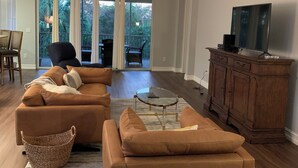 A spacious living room with a large sectional sofa, a glass coffee table, and a wooden cabinet with a flat-screen TV.