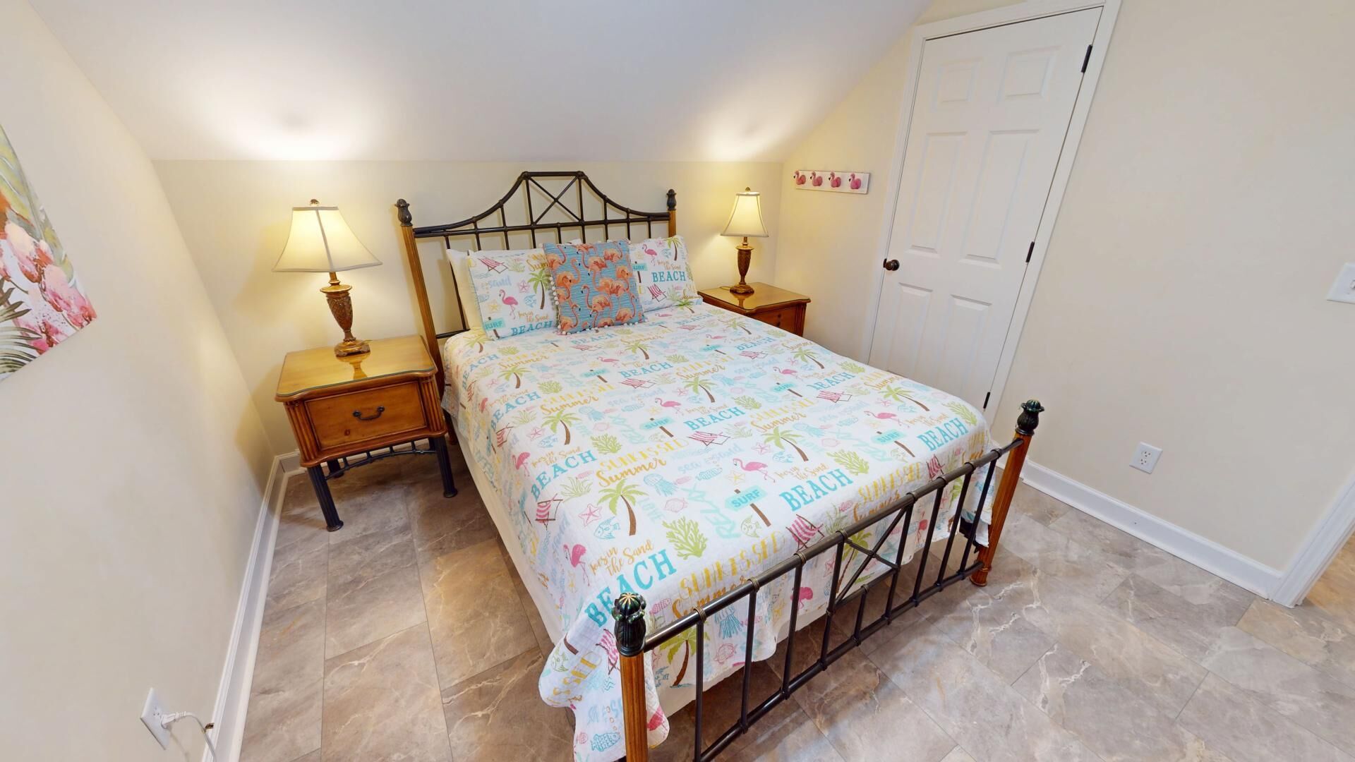 A bedroom with a bed, two bedside tables, a nightstand, a door, and a wall with a picture.
