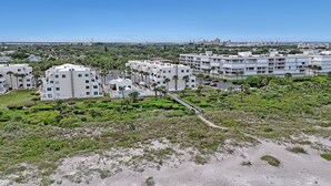 A coastal resort with multiple white buildings, a sandy beach, and a clear view of the ocean. - Heated pool, hot tub, and private beach access! (Cape Canaveral)
