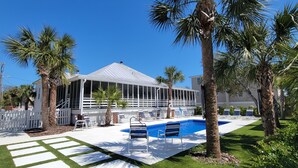 A house with a covered patio, a swimming pool, and palm trees.