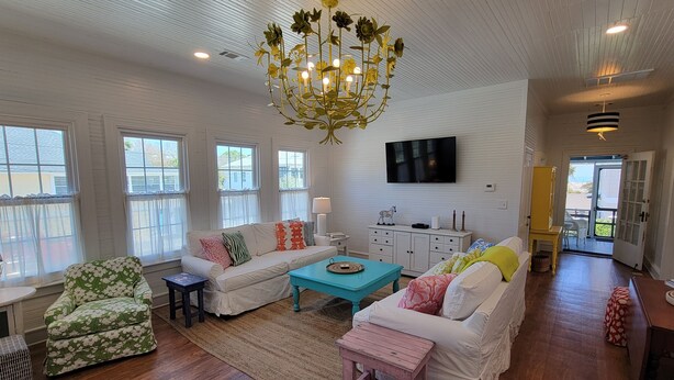A spacious living room with white walls, a large chandelier, and a television mounted on the wall.