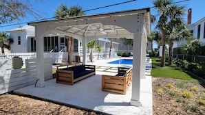A covered outdoor seating area with wooden benches and a pool in the background.