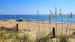 A beach with a few people, a blue umbrella, and tall grass in the foreground. - Tybee Lights 112C by Tybee Vacation Rentals (Tybee Island)