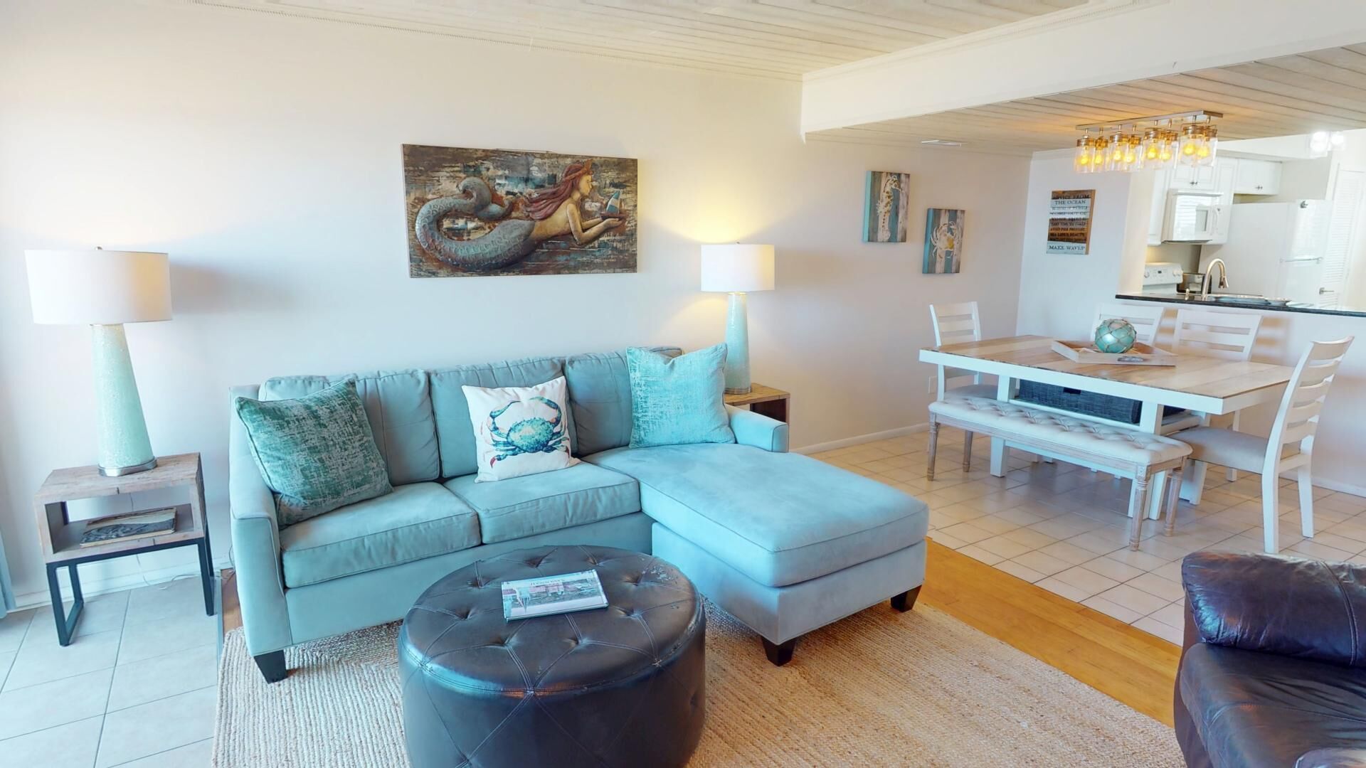 Ein modernes Wohnzimmer mit einem hellblauen Sofa, einem runden Hocker und einem Essbereich mit weißem Tisch und Stühlen.