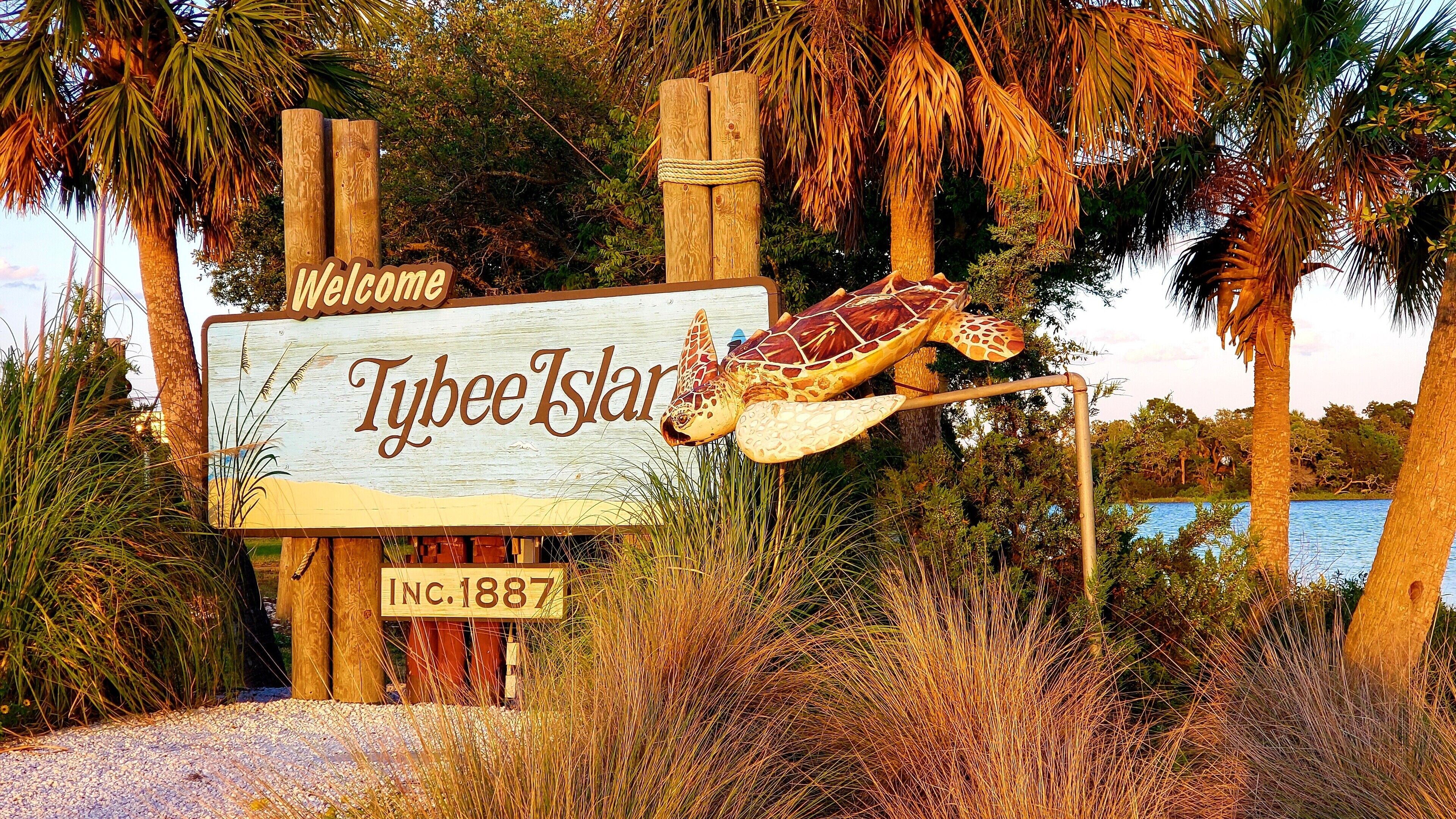 Un panneau en bois portant l’inscription « Bienvenue à Tybee Island » et « Fondée en 1887 », une sculpture de tortue et, au fond, une étendue d’eau.