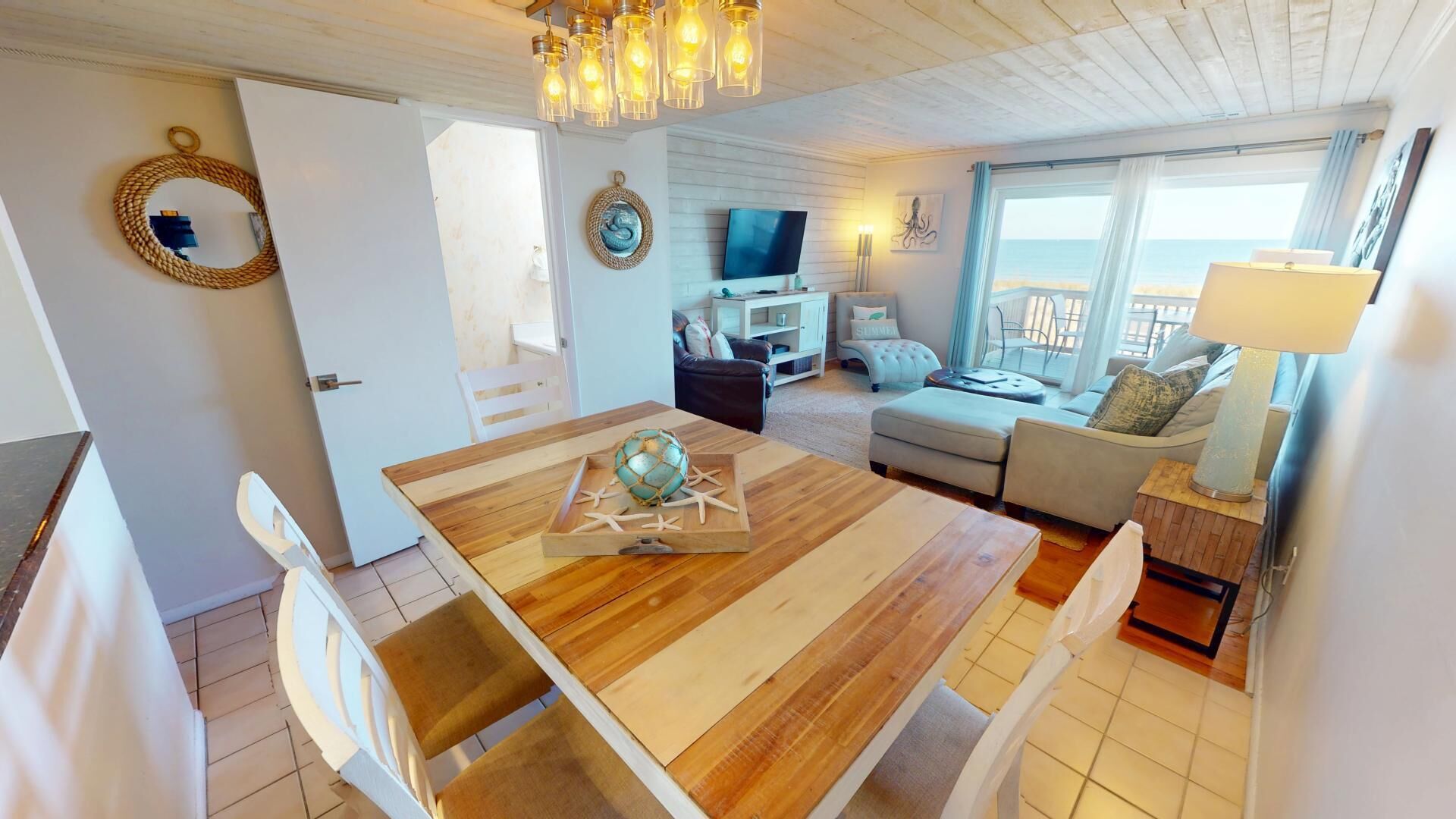 Una sala de estar acogedora con una mesa de comedor de madera, sillas blancas, un sofá y un televisor.