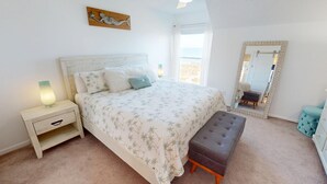 A bedroom with a bed, bedside table, bench, and a large mirror. - Tybee Lights 112C by Tybee Vacation Rentals (Tybee Island)