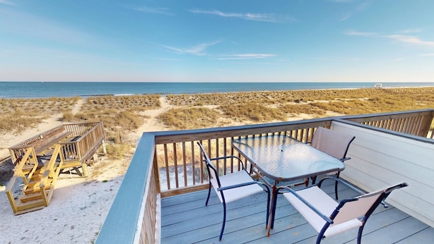 A deck with a table and chairs overlooking a beach with dunes and a clear sky. - Tybee Lights 112C by Tybee Vacation Rentals (Tybee Island)