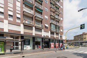 A multi-story building with balconies, a bus stop, and storefronts including a pizza place and a clothing store. - GuestHost - Modern Apartment MM3 Corvetto Milano (Milan)