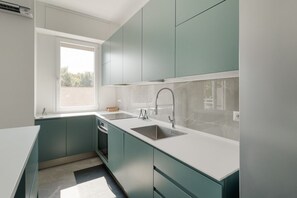 Una cocina moderna con armarios color turquesa, encimeras blancas y un ventanal que deja entrar luz natural.