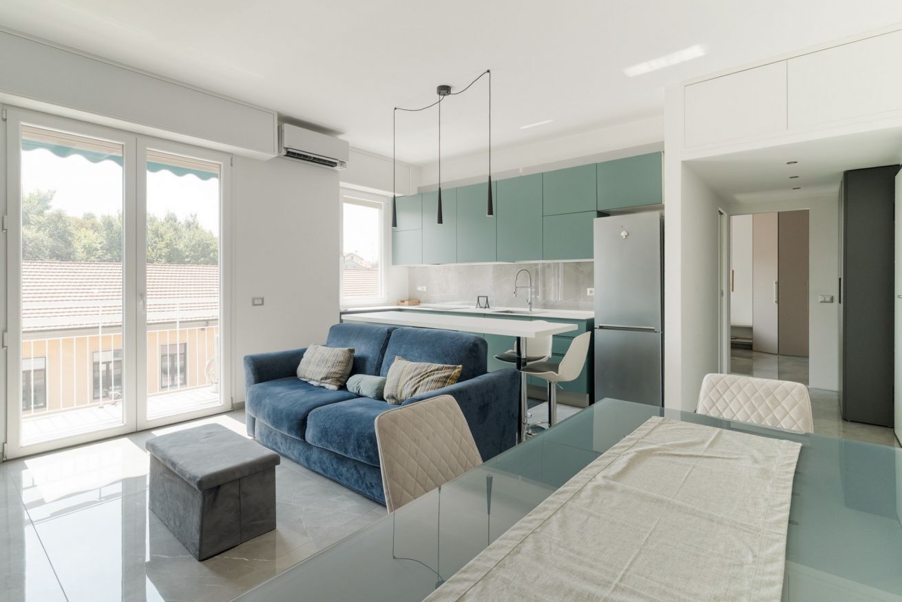 A modern kitchen with a central island, a dining area with a glass table, and a blue sofa with cushions.