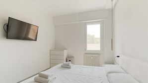 Une chambre d’hôtel moderne dotée d’un grand lit, d’un téléviseur à écran plat fixé au mur, d’une fenêtre avec stores et d’un radiateur.