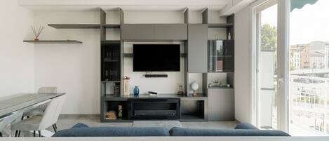 Una sala de estar moderna con televisor de pantalla plana, estanterías empotradas, una mesa de comedor y un sofá.
