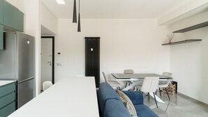 Une cuisine moderne dotée d’un réfrigérateur encastré, un coin repas avec une table et des chaises, et un canapé bleu.