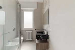 A modern bathroom with a glass shower enclosure, a white toilet, a black sink, and a window providing natural light. - GuestHost - Modern Apartment MM3 Corvetto Milano (Milan)