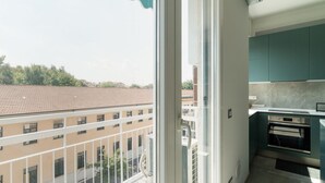 Un balcón con vistas a edificios, una ventana y una cocina con gabinetes color turquesa.