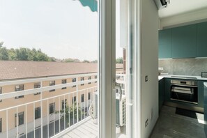 Un balcón con vistas a edificios, una ventana y una cocina con gabinetes color turquesa.