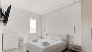 Un dormitorio moderno con una cama, mesitas de noche, un radiador, un ventanal y un televisor montado en la pared.