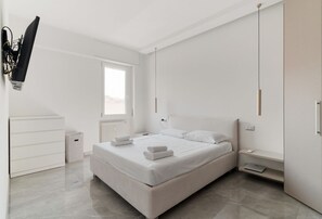 A modern bedroom with a bed, bedside tables, a radiator, a window, and a wall-mounted TV. - GuestHost - Modern Apartment MM3 Corvetto Milano (Milan)