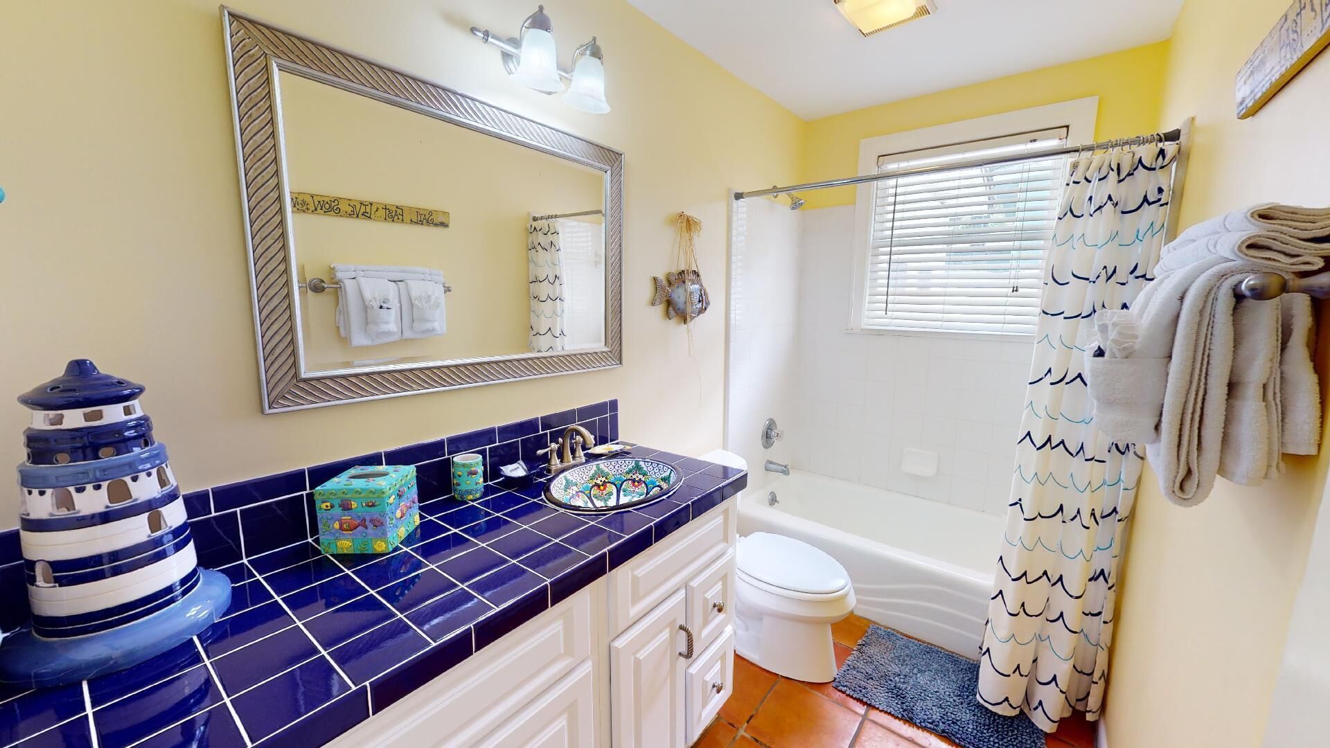 A bathroom with a blue tiled vanity, a white toilet, a bathtub, and a shower curtain with a wave pattern.