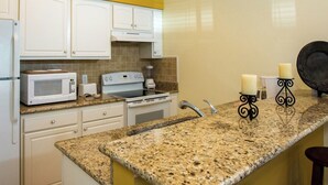 A kitchen with white cabinets, a granite countertop, a microwave, a coffee maker, and two candles on a black candle holder.