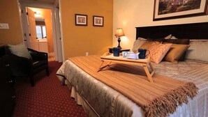 A hotel room with a bed, a chair, a tray with a lamp and a mug, and a painting on the wall.