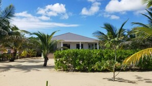 Ein Strandgrundstück mit einem eingeschossigen Haus, umgeben von Palmen und einem Sandstrand.