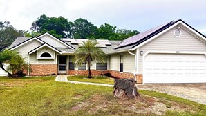 A two-story house with a garage, a front yard with a palm tree, and a brick foundation.