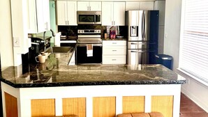 Een moderne keuken met witte kasten, een centraal eiland met krukken, roestvrijstalen apparatuur en een marmeren aanrecht.