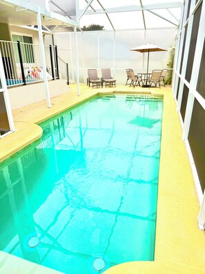Una piscina interior con superficie de agua cristalina, rodeada por una solana blanca y un recinto de vidrio.
