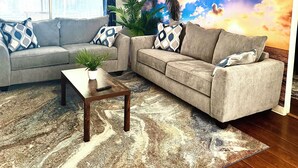A living room with a grey sofa, a coffee table, and a large tropical mural on the wall.