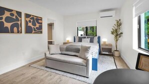 Een moderne slaapkamer met een bed, een bank, een nachtkastje, een lamp en een raam met uitzicht op groen.