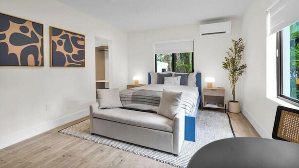 Un dormitorio moderno con cama, sofá, mesita de noche, lámpara y ventana con vistas a zonas verdes.