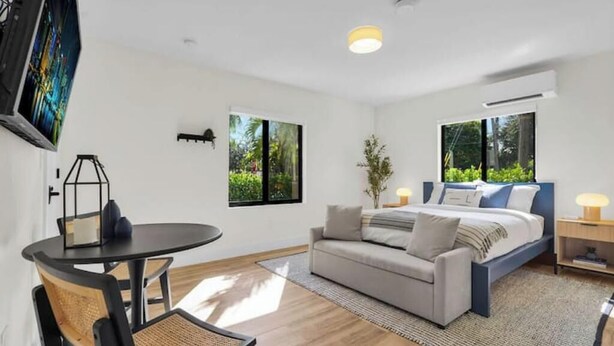 A modern bedroom with a bed, a sofa, a dining table, and a chair. There are windows with views of greenery. - My Miami Getaway, Apt 1 (Miami)