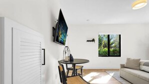 A modern living room with a round dining table, black chairs, a sofa, a mounted TV, and a window with a view of greenery. - My Miami Getaway, Apt 1 (Miami)