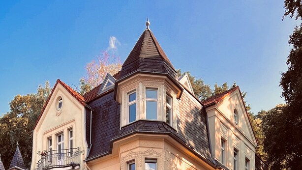 Un bâtiment historique doté d’une tourelle d’angle, de grandes baies vitrées et d’un balcon.